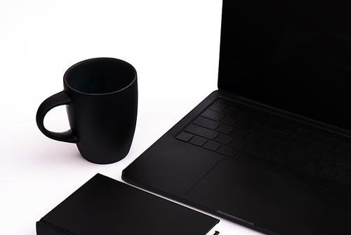 notebook and cup near black laptop on white