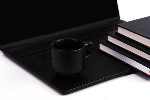 notebooks and cup near black and modern laptop isolated on white