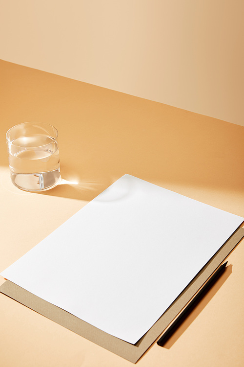 sheet of paper and pencil near glass of water on beige surface
