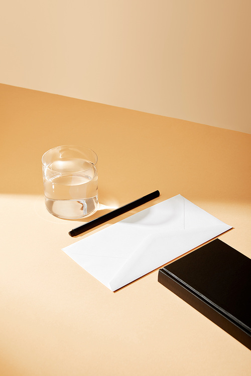 high angle view of envelope, pen, glass of water and black notebook on beige surface