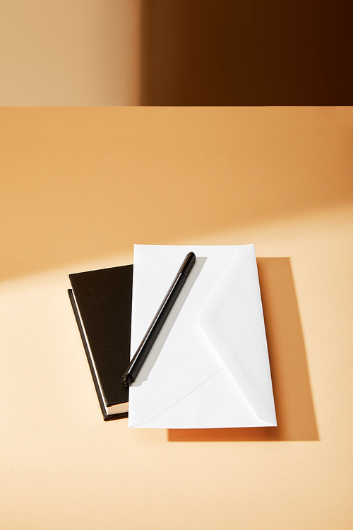 envelope, pen and black notebook on beige surface