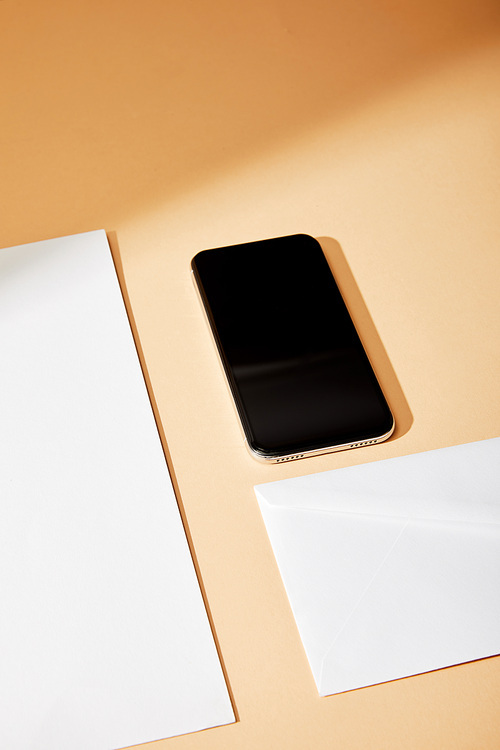 high angle view of smartphone near envelope and sheet of paper on beige background