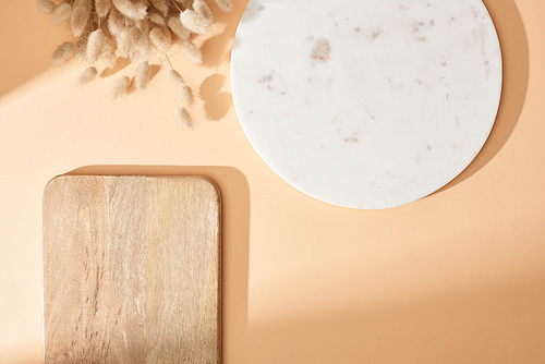 top view of marble and wooden boards near lagurus spikelets on beige background