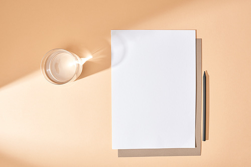 top view of sheets of paper, pencil and glass of water on beige background