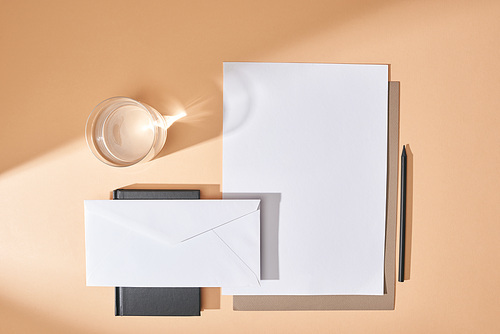 top view of sheets of paper, envelope, pen, glass of water and notebook on beige background