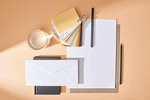 flat lay with glass of water, colors samples, sheets of paper, pens, envelope and notebook on beige background