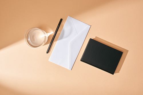 top view of envelope, pen, glass of water and black notebook on beige background