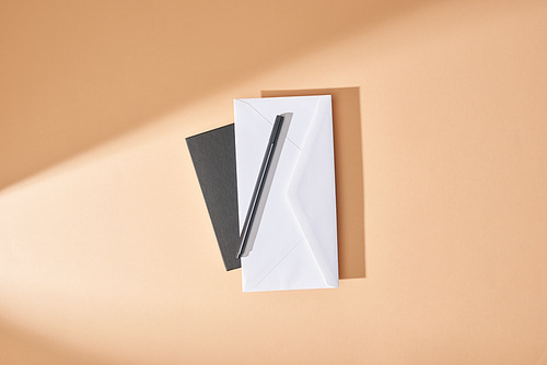 top view of envelope and pen on notebook on beige background