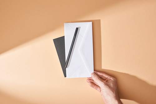 partial view of man holding envelope and pen near notebook on beige background