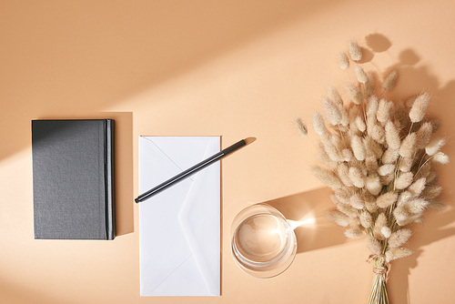top view of notebook, envelope, pen, glass of water and lagurus spikelets on beige background