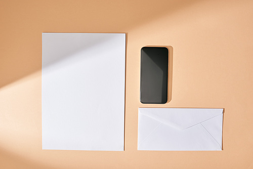 top view of sheet of paper, smartphone and envelope on beige background