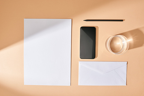 flat lay with sheet of paper, smartphone, pencil, glass of water and envelope on beige background