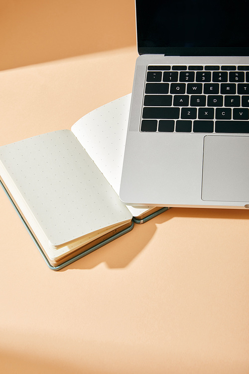 high angle view of opened blank notebook and laptop on beige background