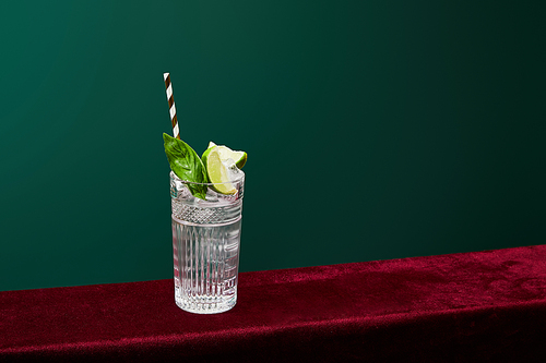 high angle view of mojito with ice, mint, lime and striped  straw in collins glass isolated on green