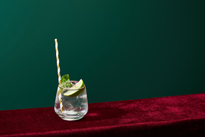 high angle view of old fashioned glass with golden rim with mojito and striped  straw isolated on green