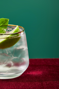 Close up view of cropped glass with refreshing mojito, mint and lime slice isolated on green