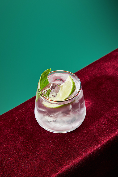 High angle view of glass with fresh mojito, mint and lime slice on green and black background