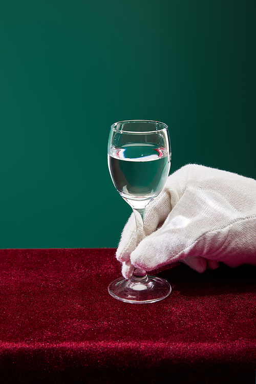 Cropped view of hand in terry glove holding shot glass with liquid isolated on green