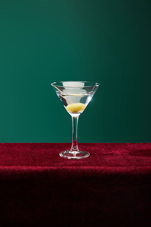 Crystal cocktail glass with vermouth and whole olive on toothpick isolated on green