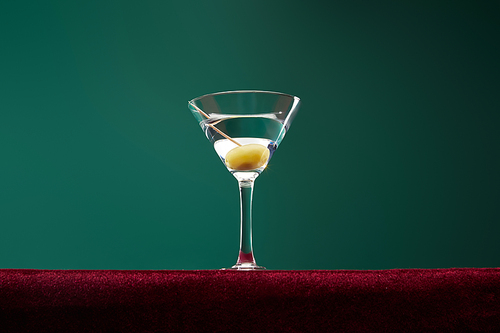 Low angle view of cocktail glass with vermouth and whole olive on toothpick isolated on green