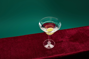 High angle view of cocktail glass with vermouth and whole olive on toothpick isolated on green