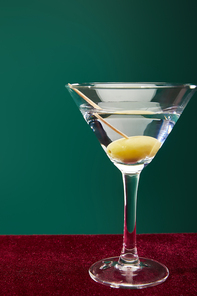close up view of cocktail glass with vermouth and whole olive on toothpick isolated on green
