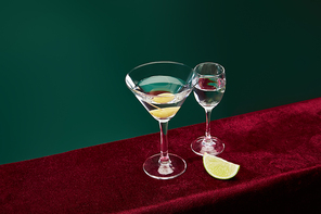 high angle view of shot glass and cocktail glass with vermouth and whole olive on toothpick on velour surface isolated on green