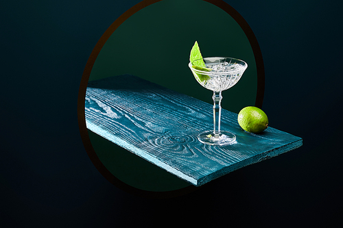 high angle view of cocktail glass with mint leaf and whole lime on blue wooden surface on geometric background