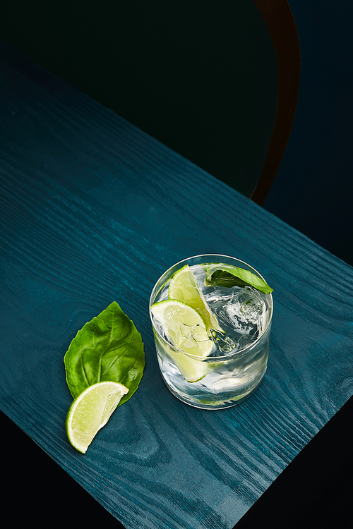 Top view of old fashioned glass with fresh drink, mint leaf and lime slice on blue wooden surface isolated on black