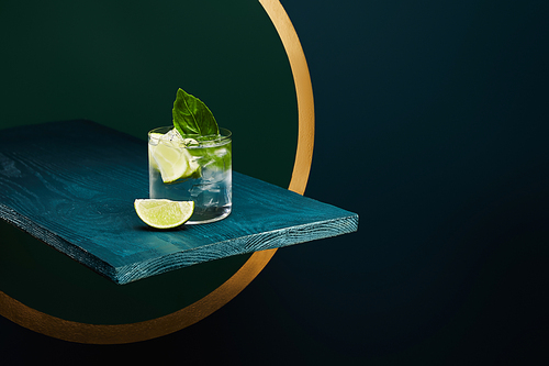 Glass with refreshing drink with, ice, mint leaf and lime slice on wooden surface on geometric blue and green background