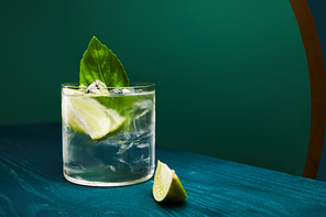 close up view of old fashioned glass with drink and lime on blue wooden surface isolated on green