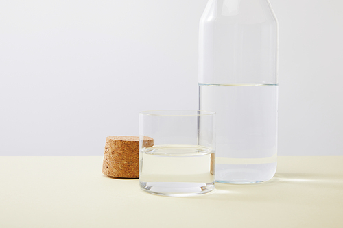 Close up view of bottle, cork and glass filled with water isolated on grey