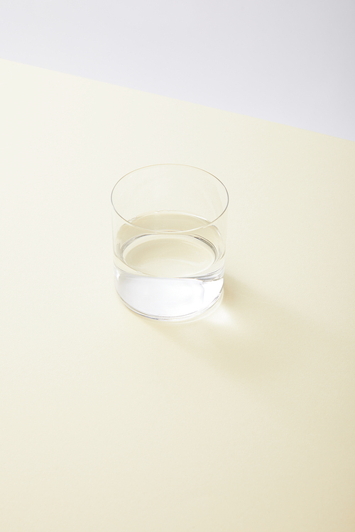 high angle view of glass with water on yellow surface isolated on grey
