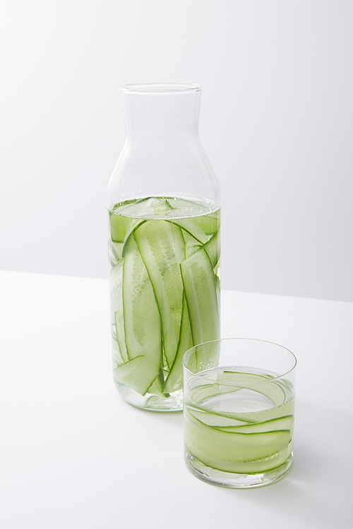 high angle view of bottle and glass with water and sliced cucumbers isolated on grey