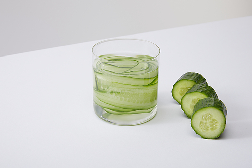 high angle view of glass with fresh drink and sliced cucumbers isolated on grey