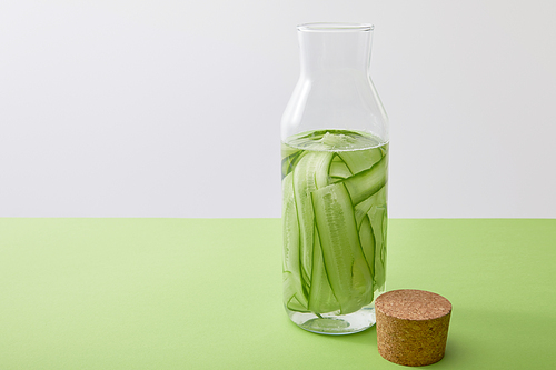 Cork and bottle with water and sliced cucumbers isolated on grey