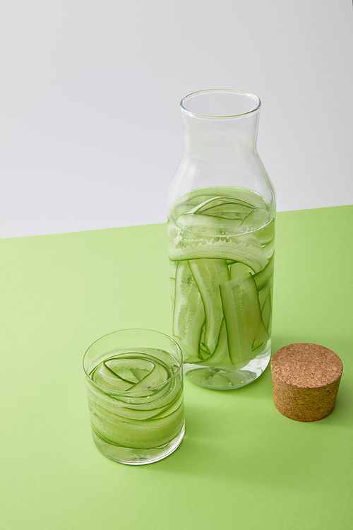 high angle view of cork, glass and bottle with water and sliced cucumbers                isolated on grey