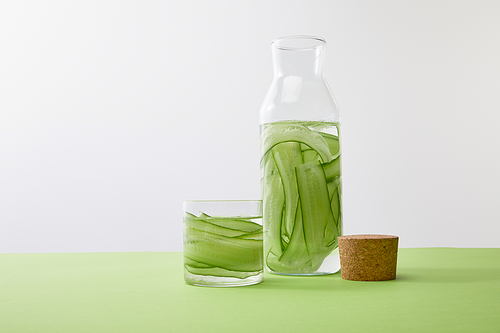 Bottle and glass with drink made of sliced cucumbers isolated on grey