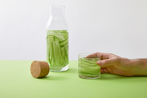 Cropped view of male hand holding glass with drink made of sliced cucumbers isolated on grey