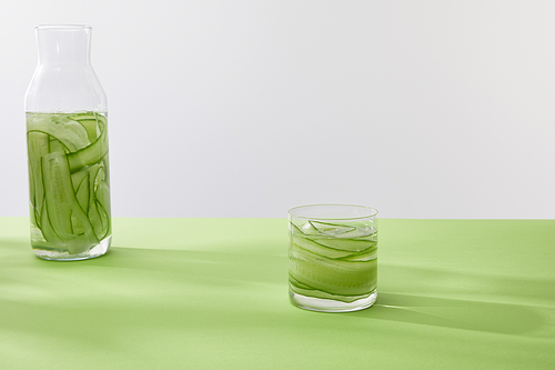 Bottle and glass with drink made of sliced cucumbers on green surface isolated on grey