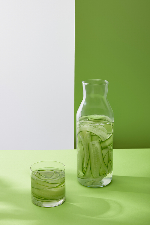 high angle view of bottle and glass with drink made of sliced cucumbers on grey and green background