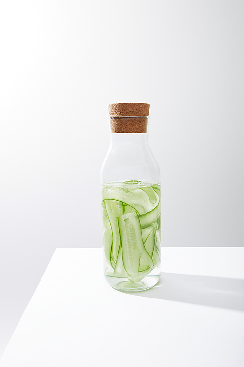 Glass bottle with cork and drink made of sliced cucumbers isolated on grey
