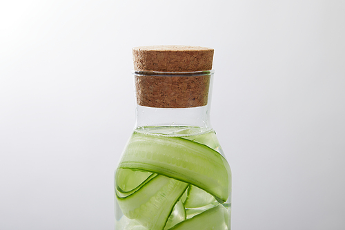 Close up view of glass bottle with cork with drink made of sliced cucumbers isolated on grey
