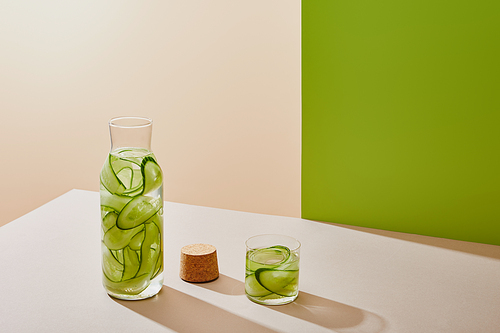 high angle view of cork, glass and bottle filled with water and sliced cucumbers on table on beige and green background