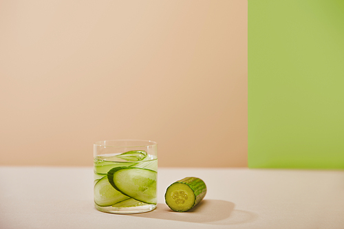 Glass of detox drink and sliced cucumbers on beige and green background