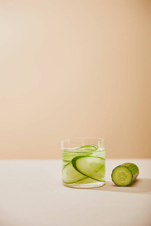 Glass of water with sliced cucumbers on table isolated on beige