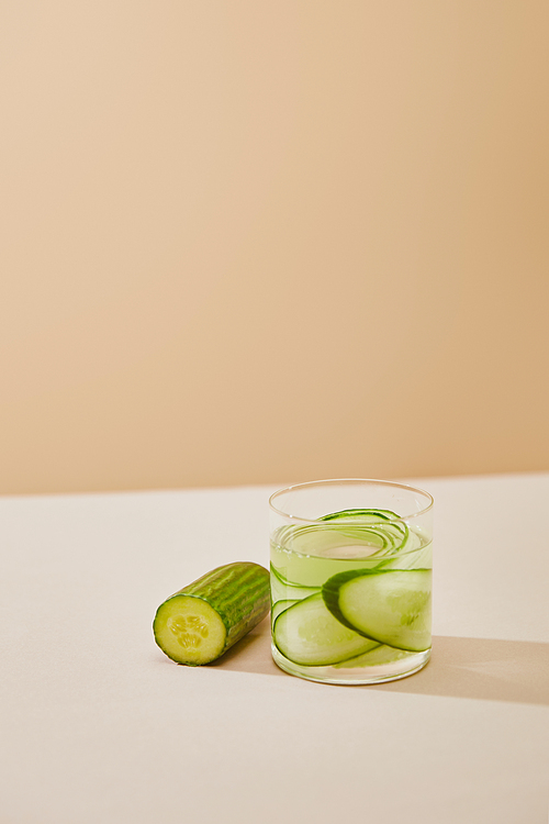 high angle view of glass of water with sliced cucumbers on table isolated on beige