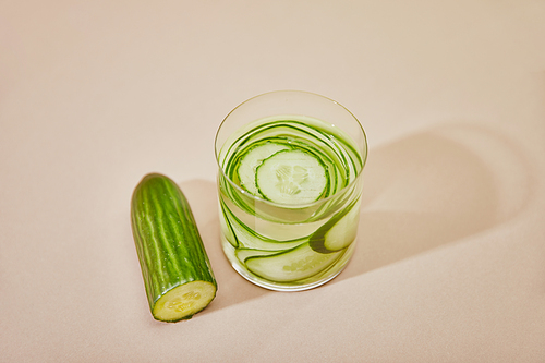 High angle view of glass with detox drink and sliced cucumbers on table on beige background
