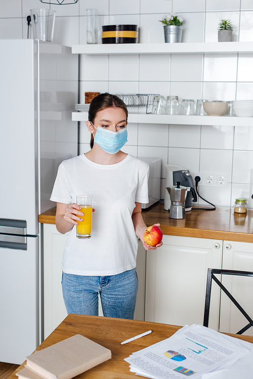 young woman in medical mask holding glass of orange juice and apple