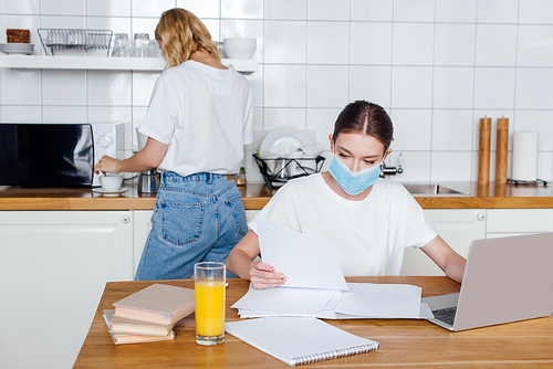 freelancer in medical mask near books, laptop, glass of orange juice and sister